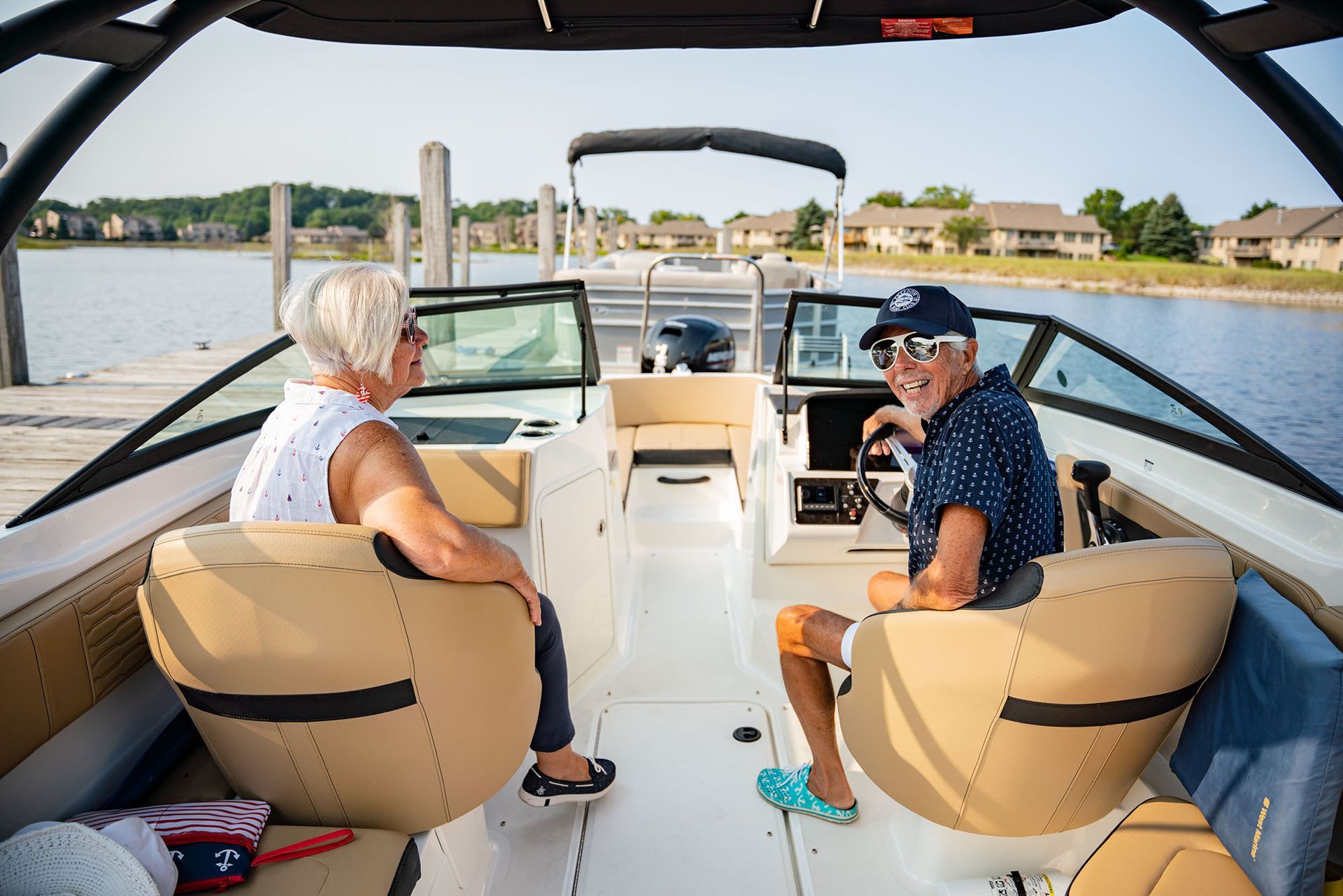 Two people smiling on a boat. Man at the helm, woman in passenger seat, on a lake.