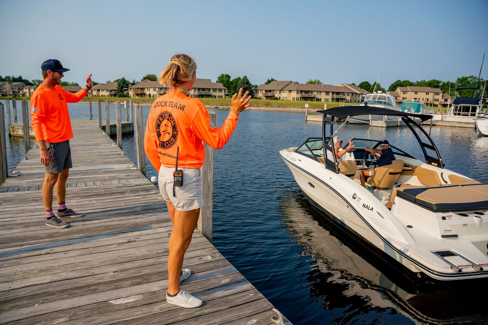 Two marina workers wave to a boat departing the dock.