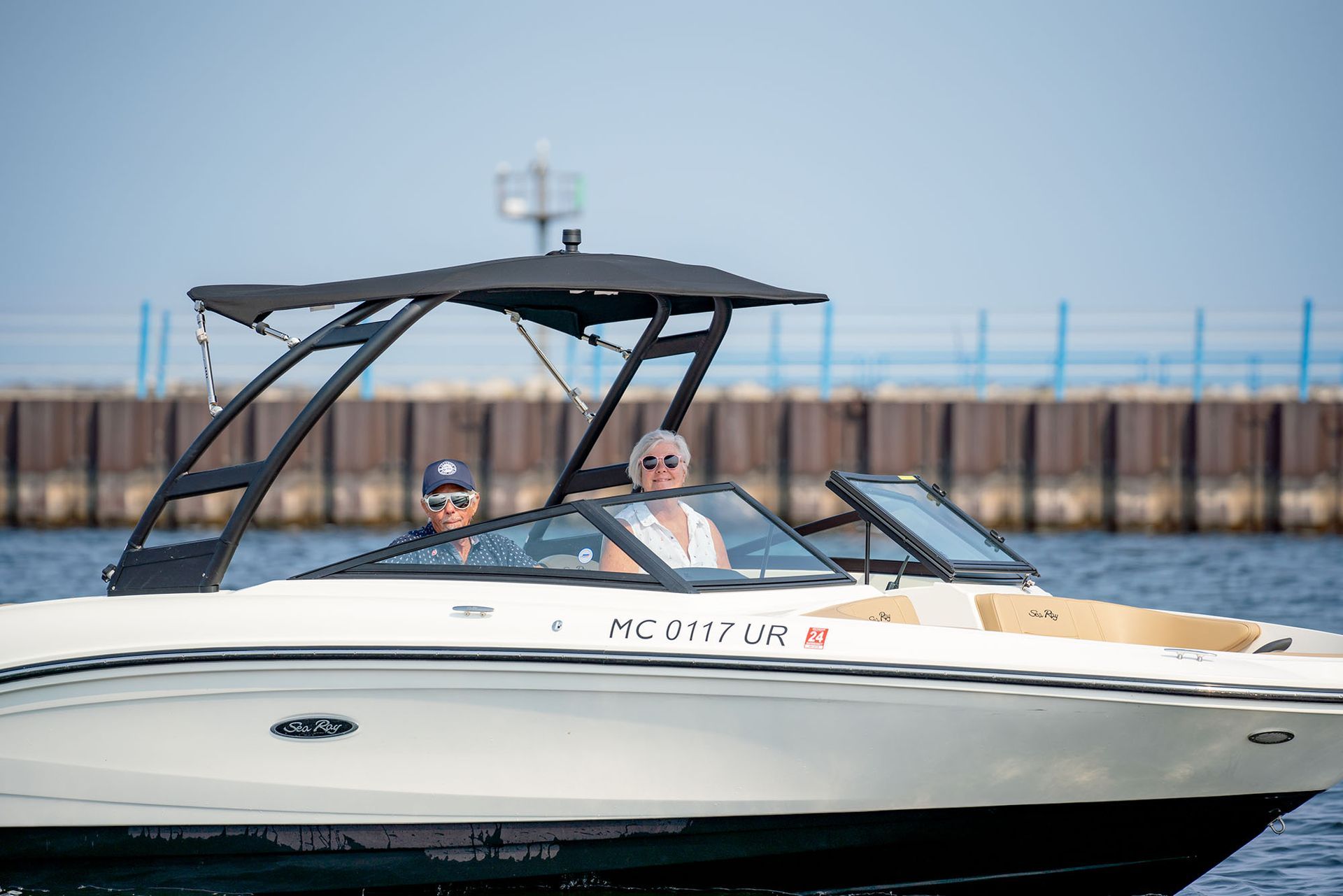 Two people on a white motorboat with a black canopy on a lake.