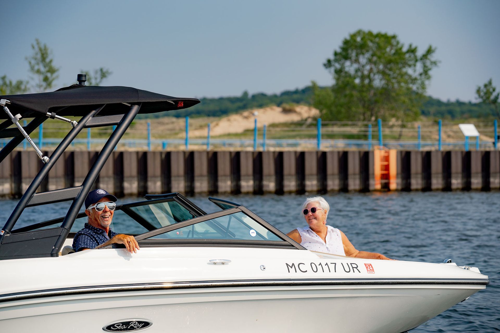 Elderly couple on a white motorboat, cruising a lake. Bright sunlight, calm water.