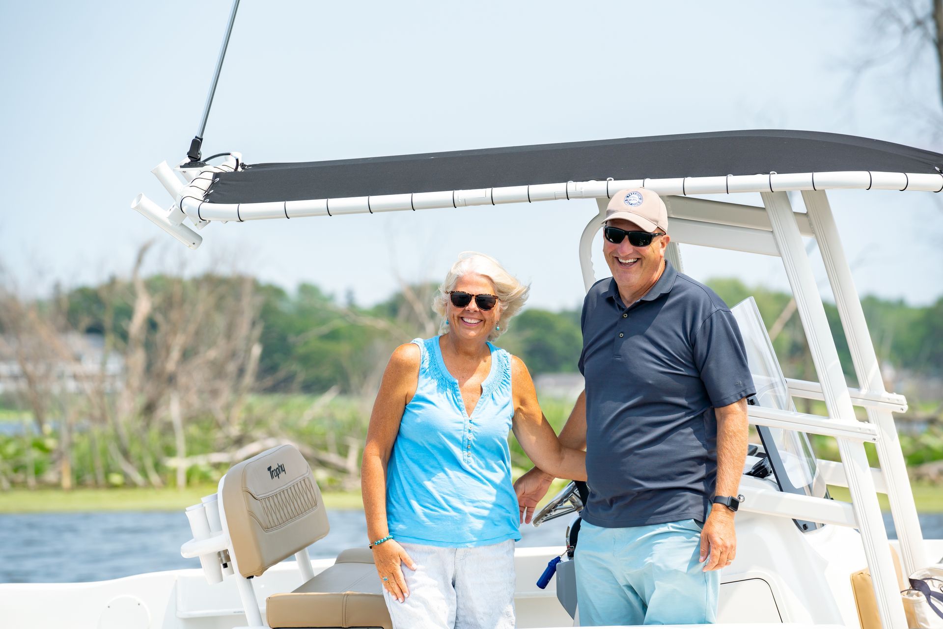 Smiling couple on a boat, blue sky and water. Woman in blue, man in navy, sunny day.