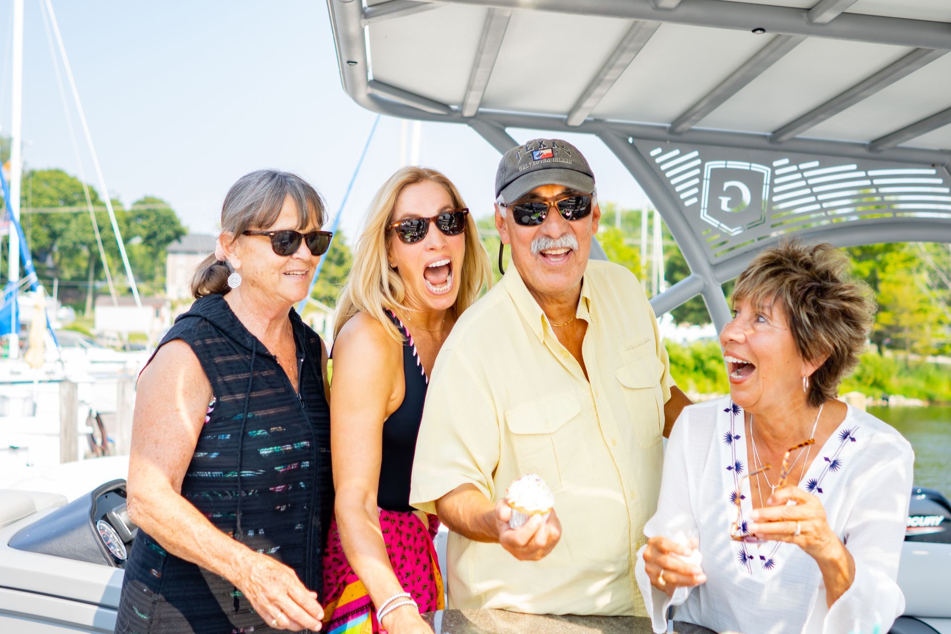 Four people on a boat with surprised expressions, one holding something, sunny outdoor setting.