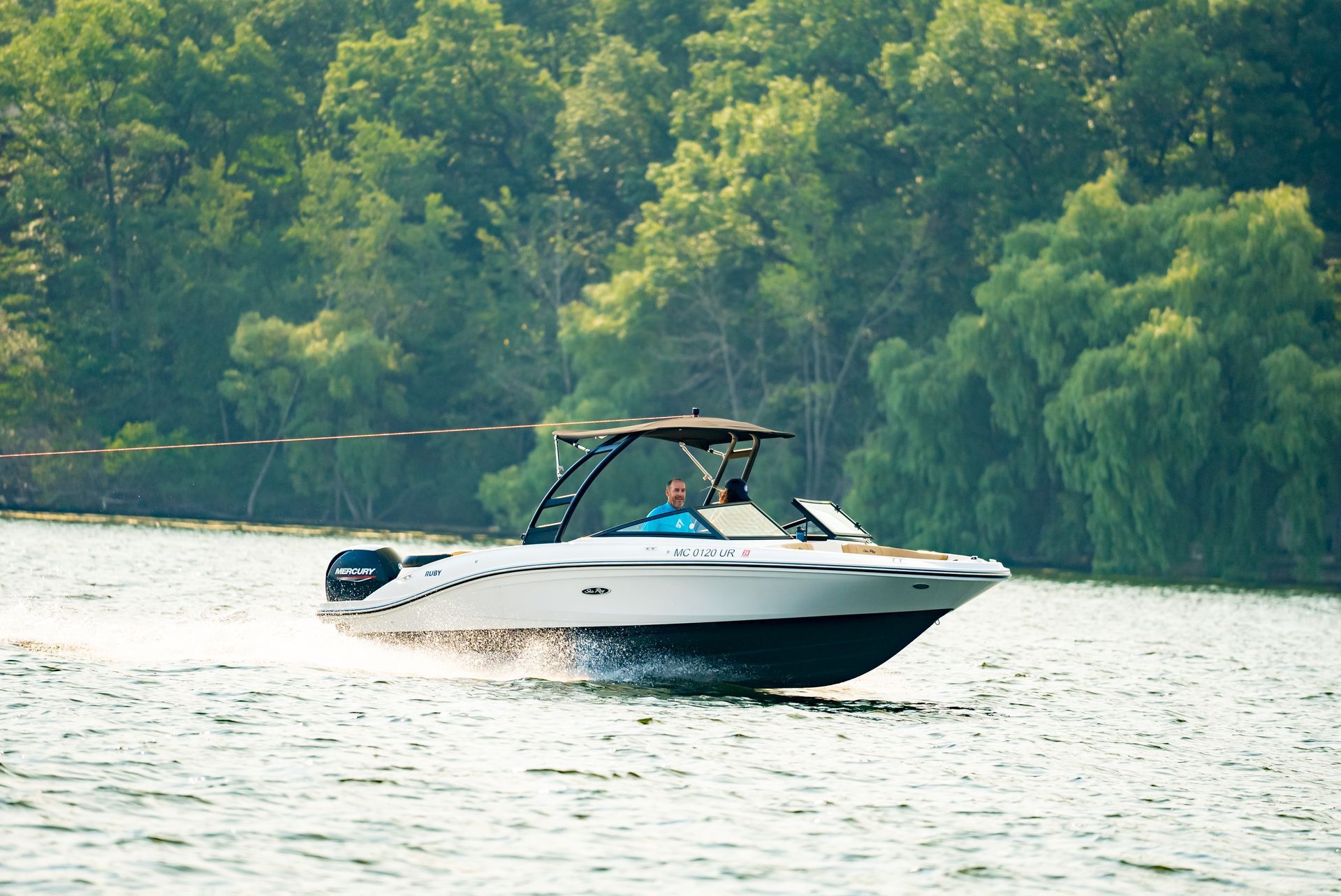 White motorboat on water, person at helm, trees in background.