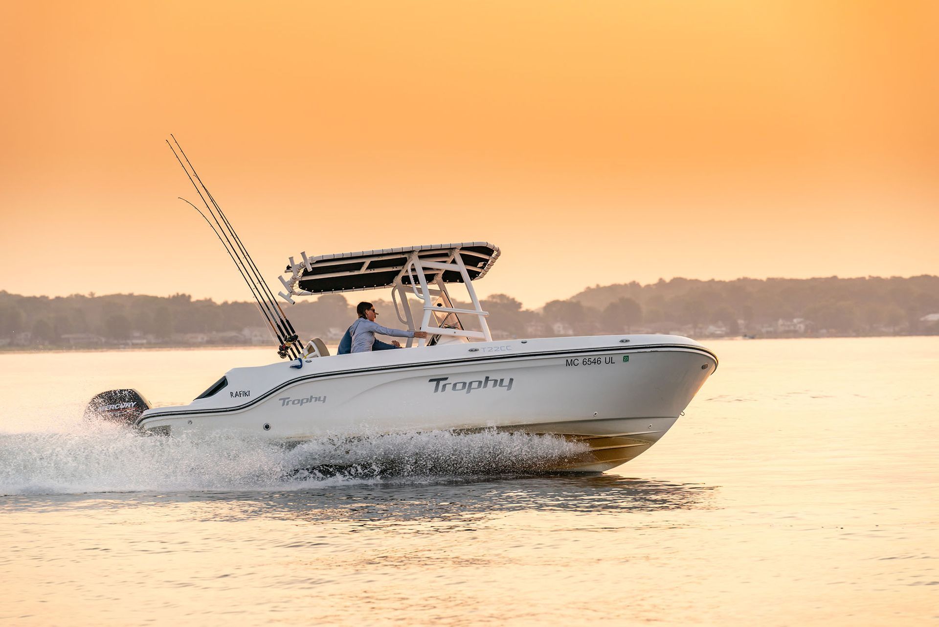 White motorboat speeding on water at sunset; man at the helm.
