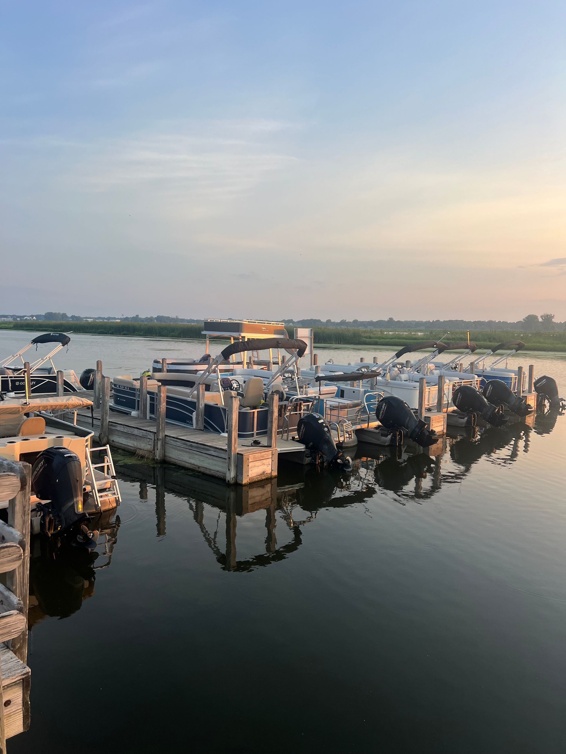 Boats docked in a harbor, reflecting in the water at dusk; blue, white, and gray hues dominate.