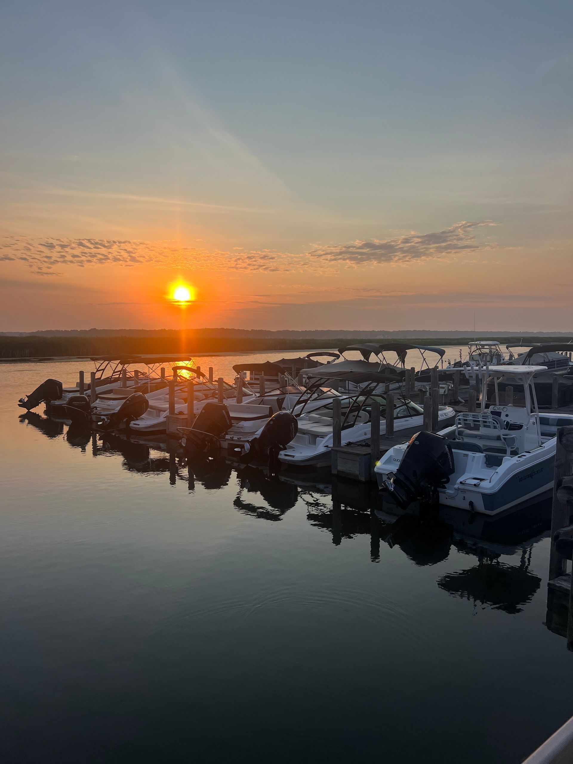 Sunset over a harbor with boats docked; orange sun reflects on water and boats.