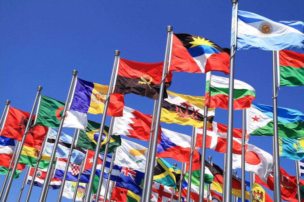 Flags of various nations waving in the wind against a clear blue sky.