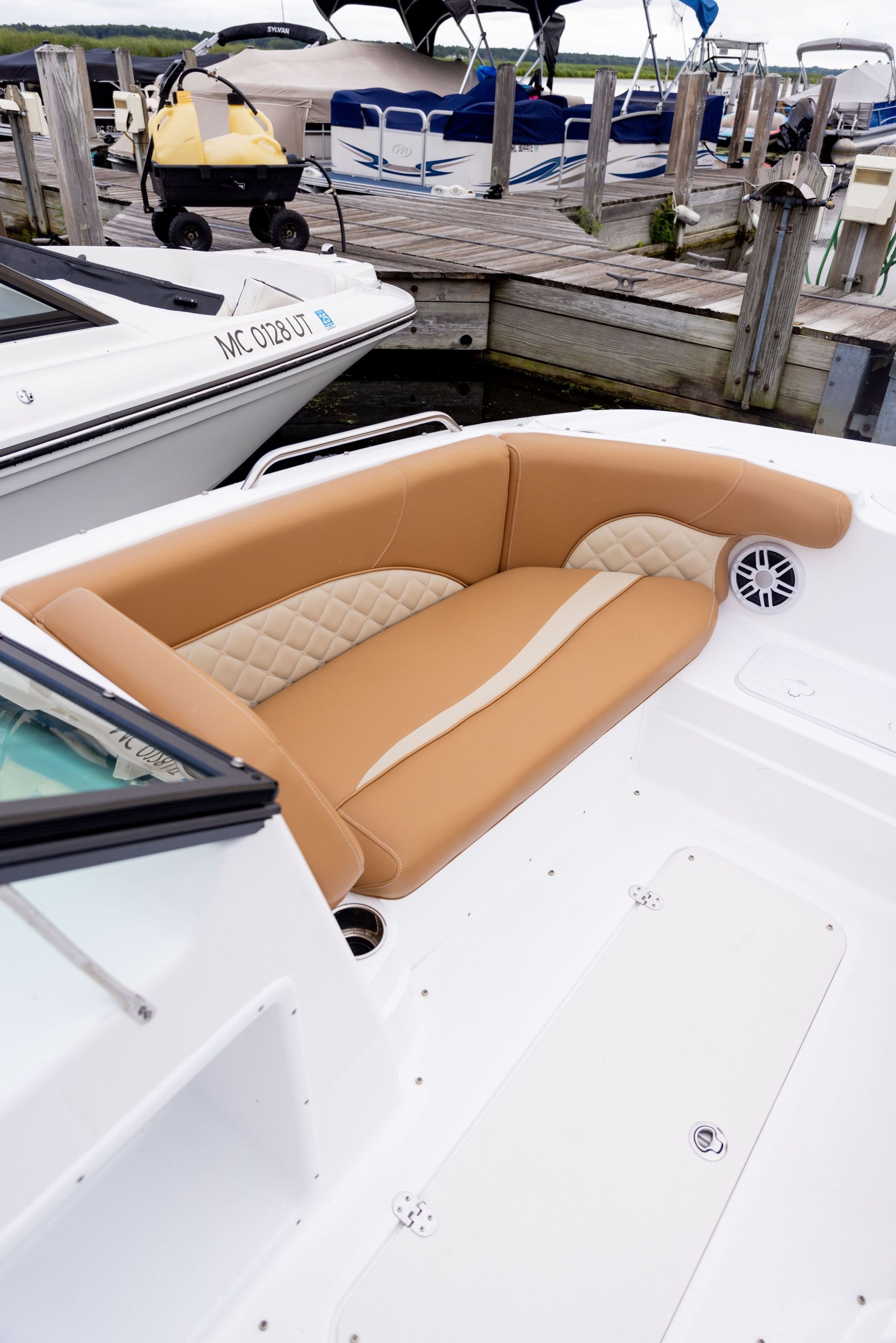 A white boat with a brown seat is docked at a dock.