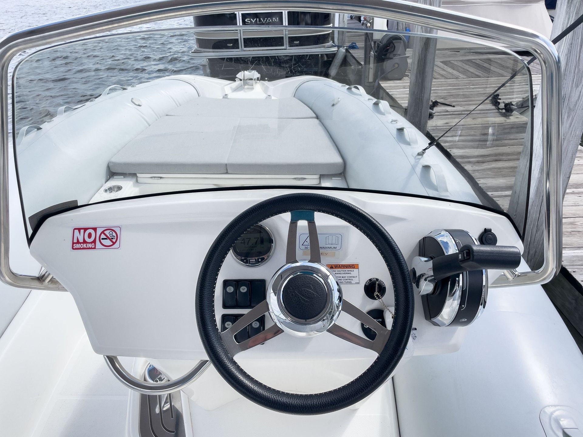 A white boat with a steering wheel and windshield is docked at a dock.