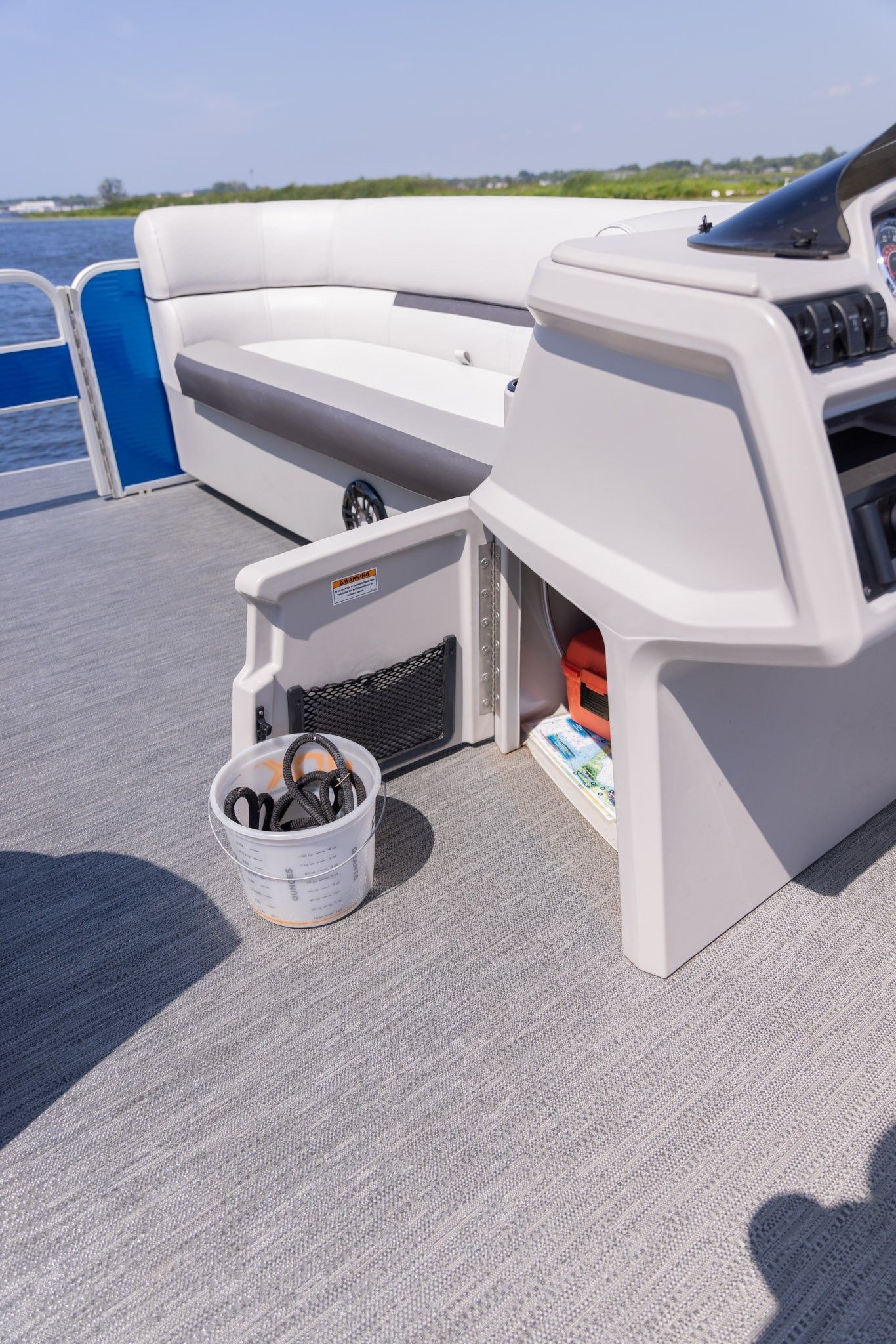 A pontoon boat with a bucket of fishing gear on the deck.