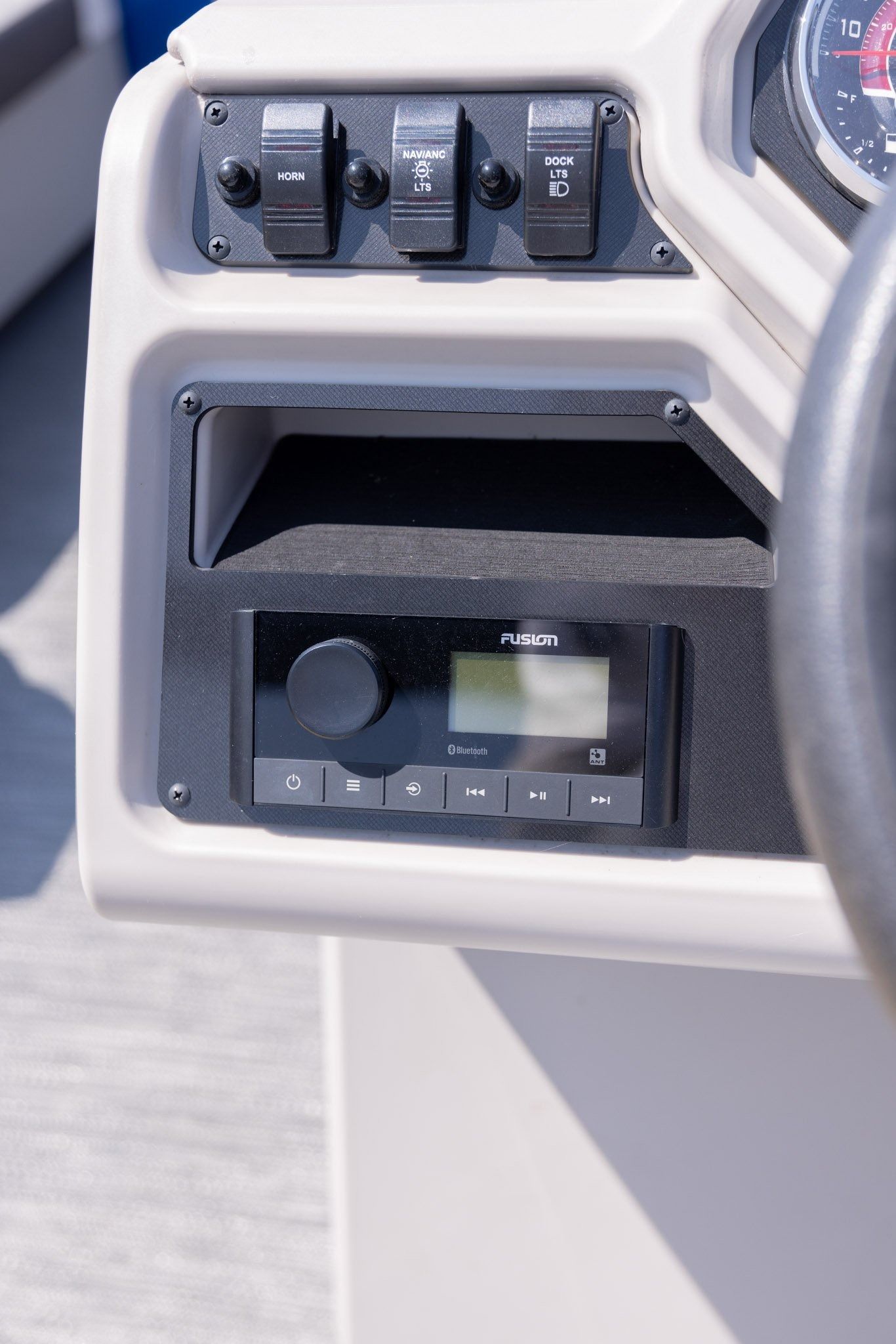 A close up of a boat dashboard with a steering wheel and a radio.