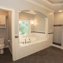Luxury bathroom with a large soaking tub, arched window, tiled floor, and beige walls