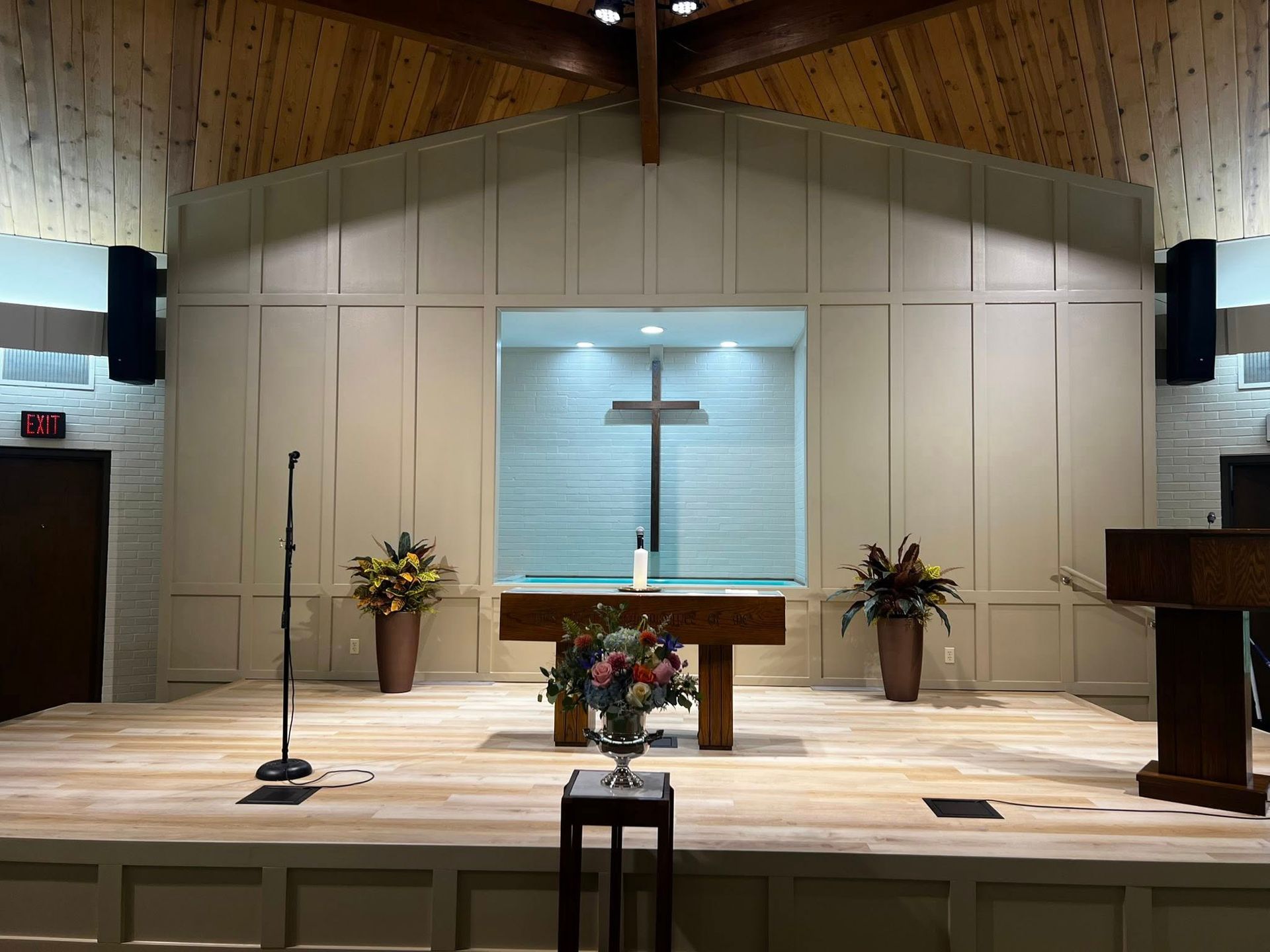 Church sanctuary with altar, cross, lectern, microphones, and floral arrangements at the front