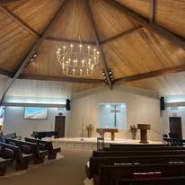 Interior of a church sanctuary with wooden vaulted ceiling, chandelier, pews, and altar at the front.