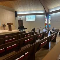 Empty church sanctuary with wooden pews, pulpit, and projector screen on the front wall