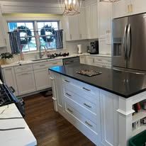 Bright modern kitchen with white cabinets, black island countertop, and stainless steel refrigerator