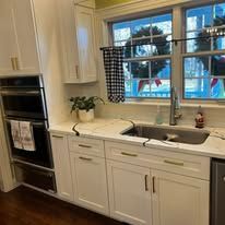 Bright white kitchen with double oven, sink, window, and blue outdoor view