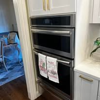 Built-in stainless steel oven and microwave in a white kitchen, with dish towels on the oven door.