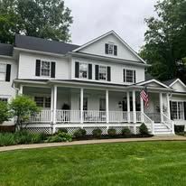 White two-story house with a front porch, black shutters, and an American flag on a green lawn.