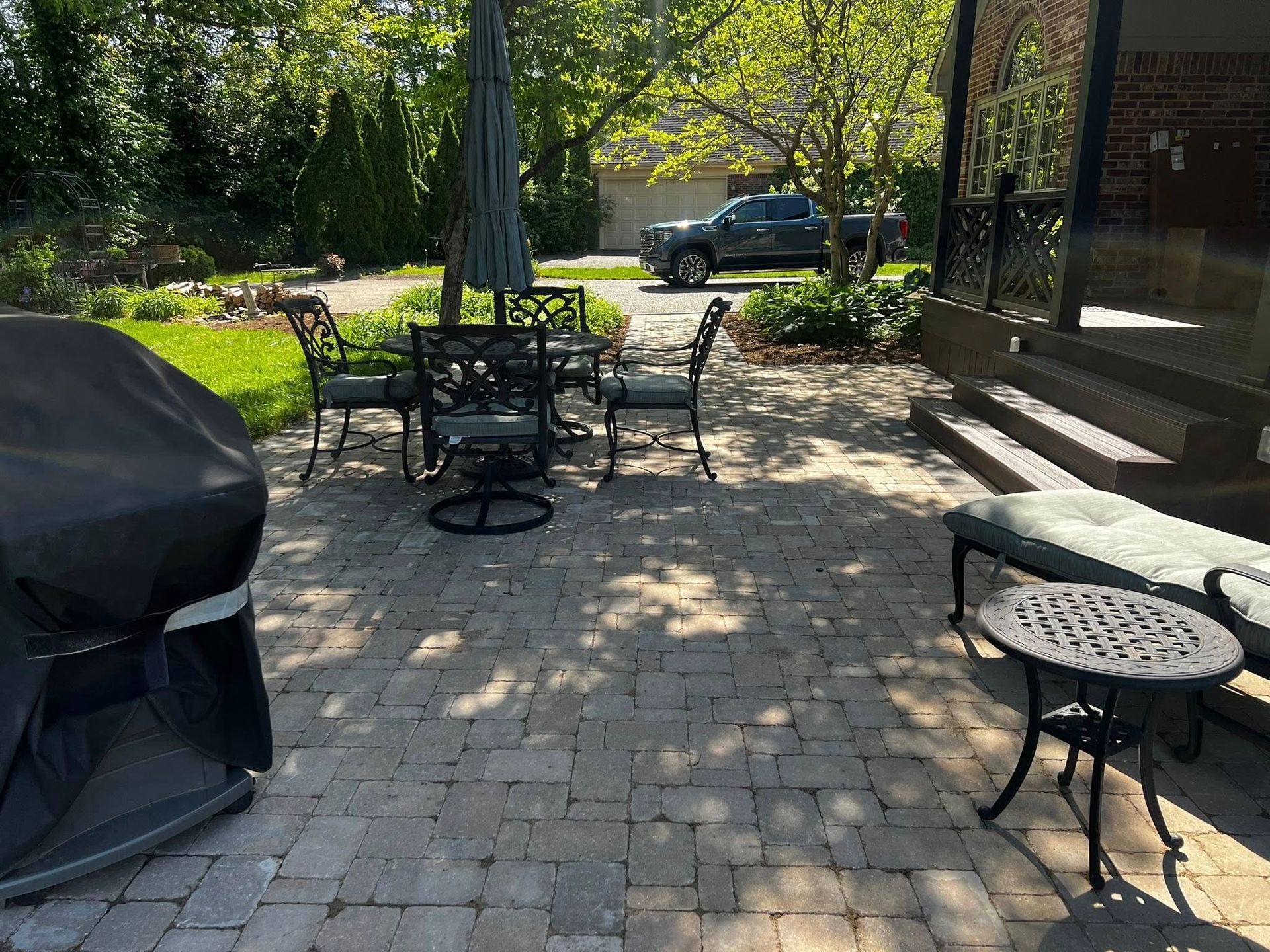 Covered porch with wooden railing and steps beside a brick house and paved patio