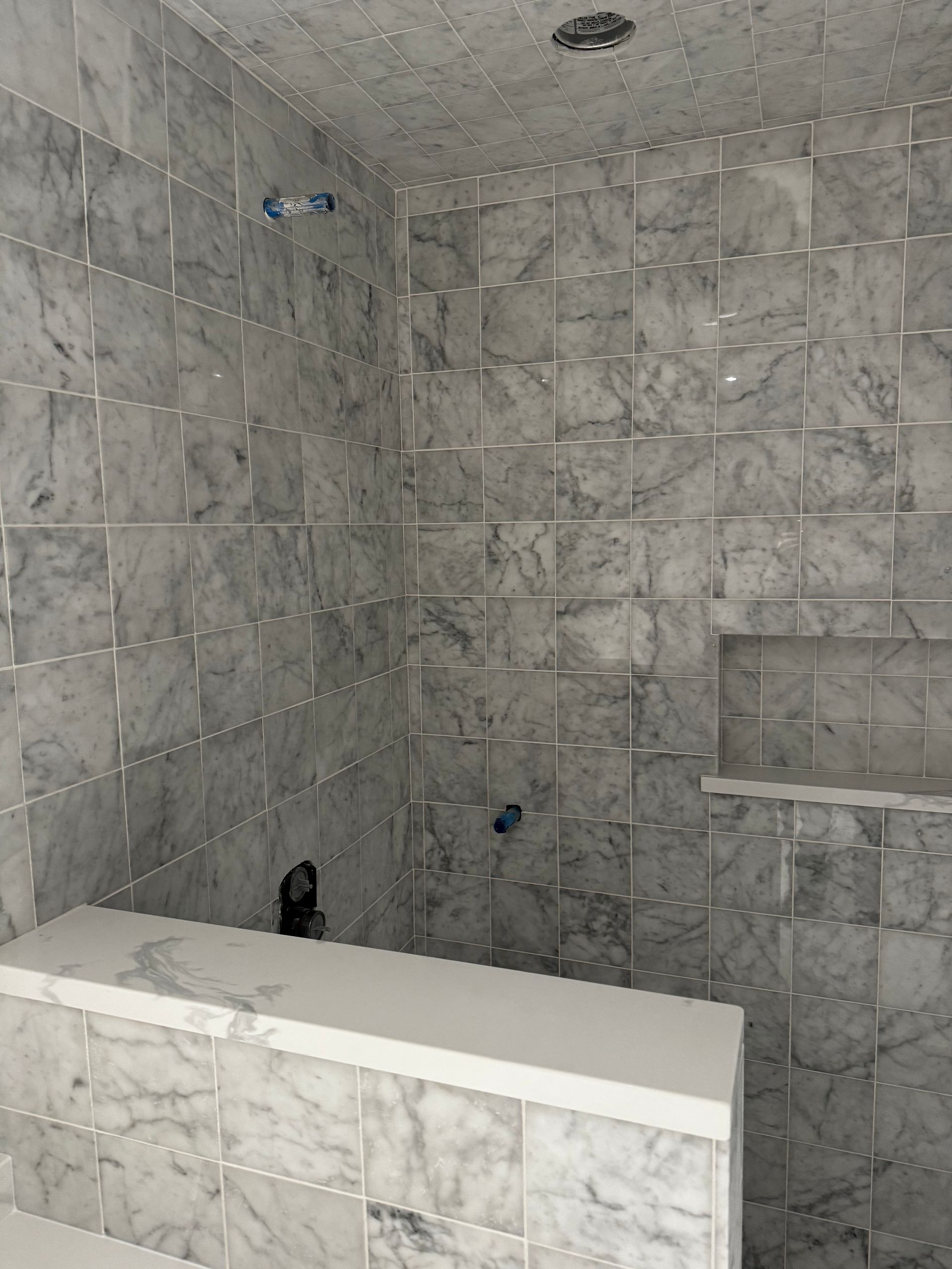 Empty tiled shower stall with gray marble-look walls and a built-in ledge.