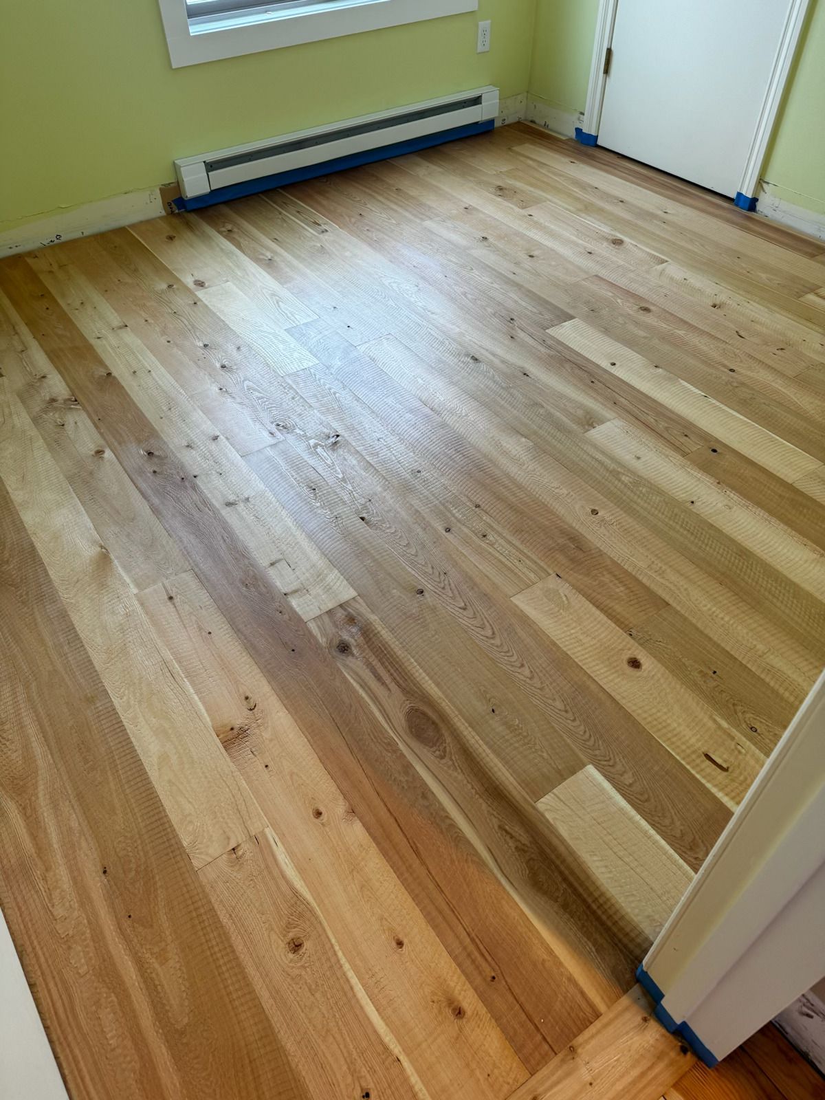 Empty room with light wood floor, yellow walls, baseboard heater, and white door trim.