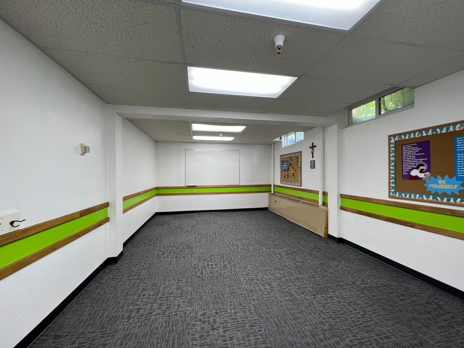Empty office hallway with white walls, green stripe trim, carpeted floor, and fluorescent ceiling lights.