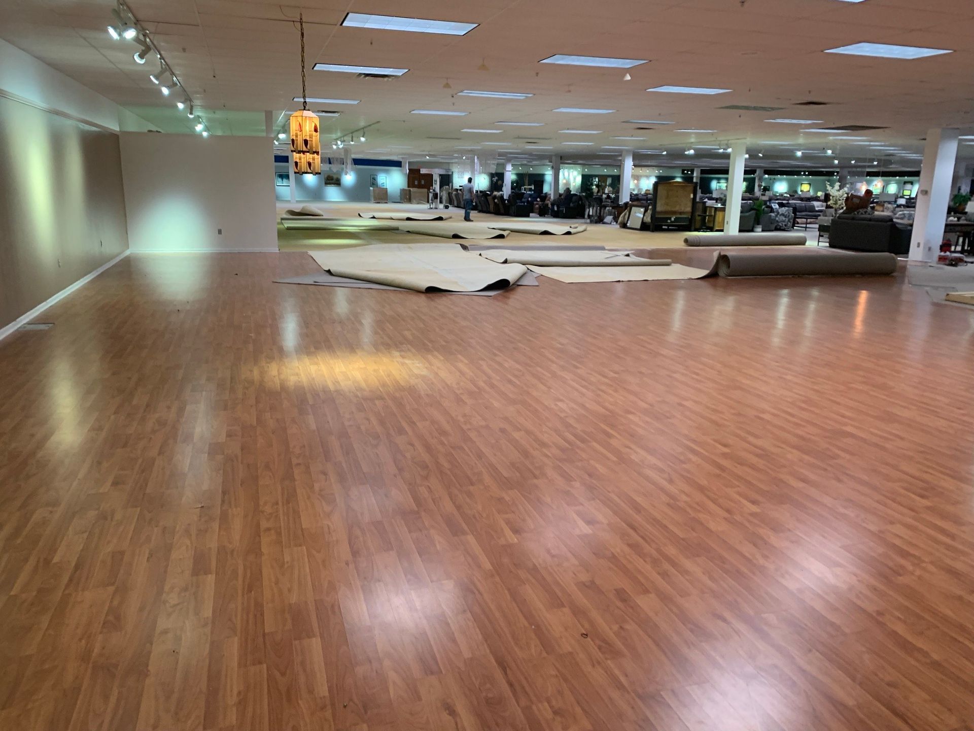 Empty indoor gym with polished wooden floor, overhead lights, and mirrors along the far wall