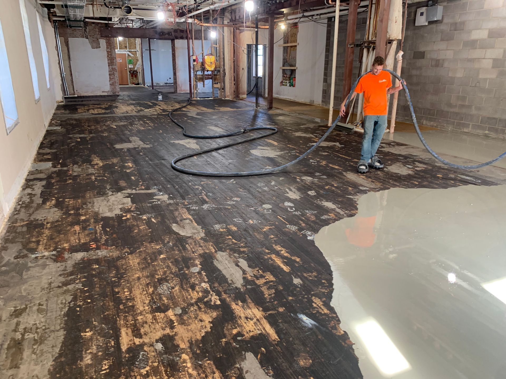 Construction workers sanding a damaged floor in a gutted room, with dust and exposed walls.