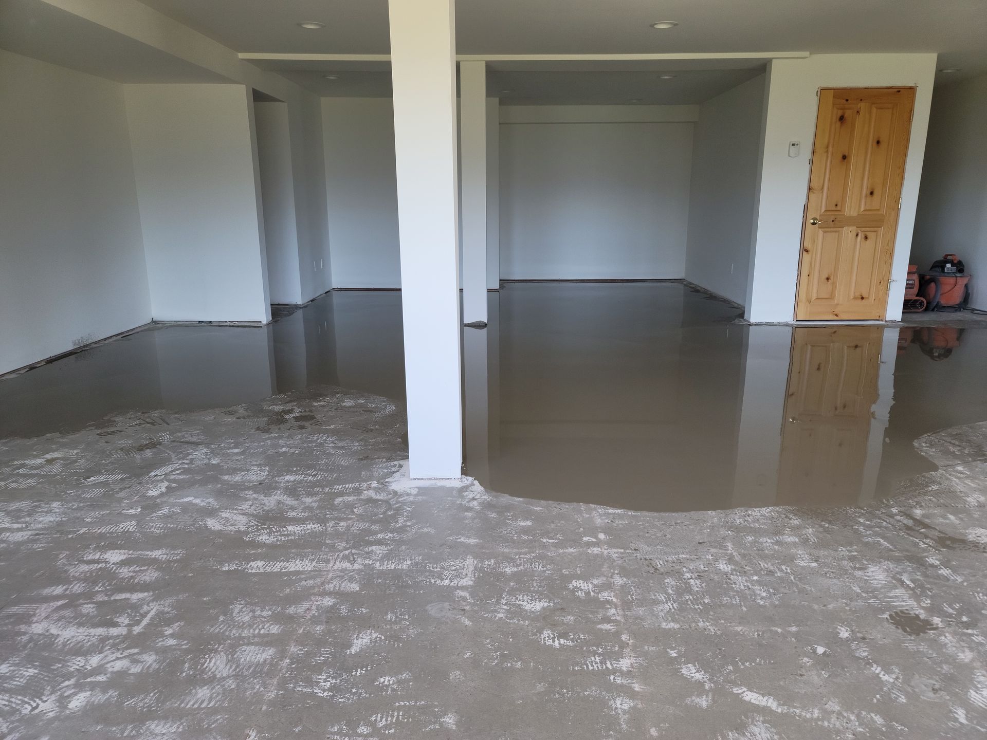 Empty room with glossy gray floor, white columns, and a wooden door on the right.