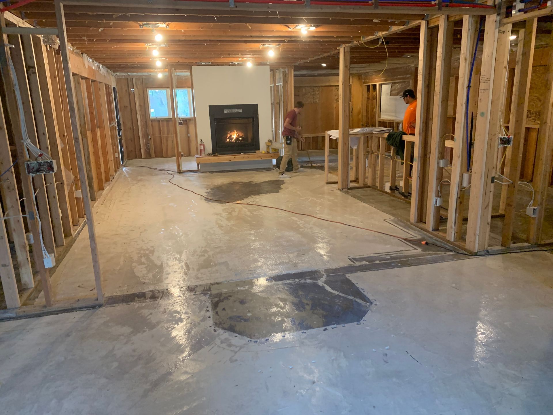 Unfinished basement with exposed framing, concrete floor, and a fireplace under construction.