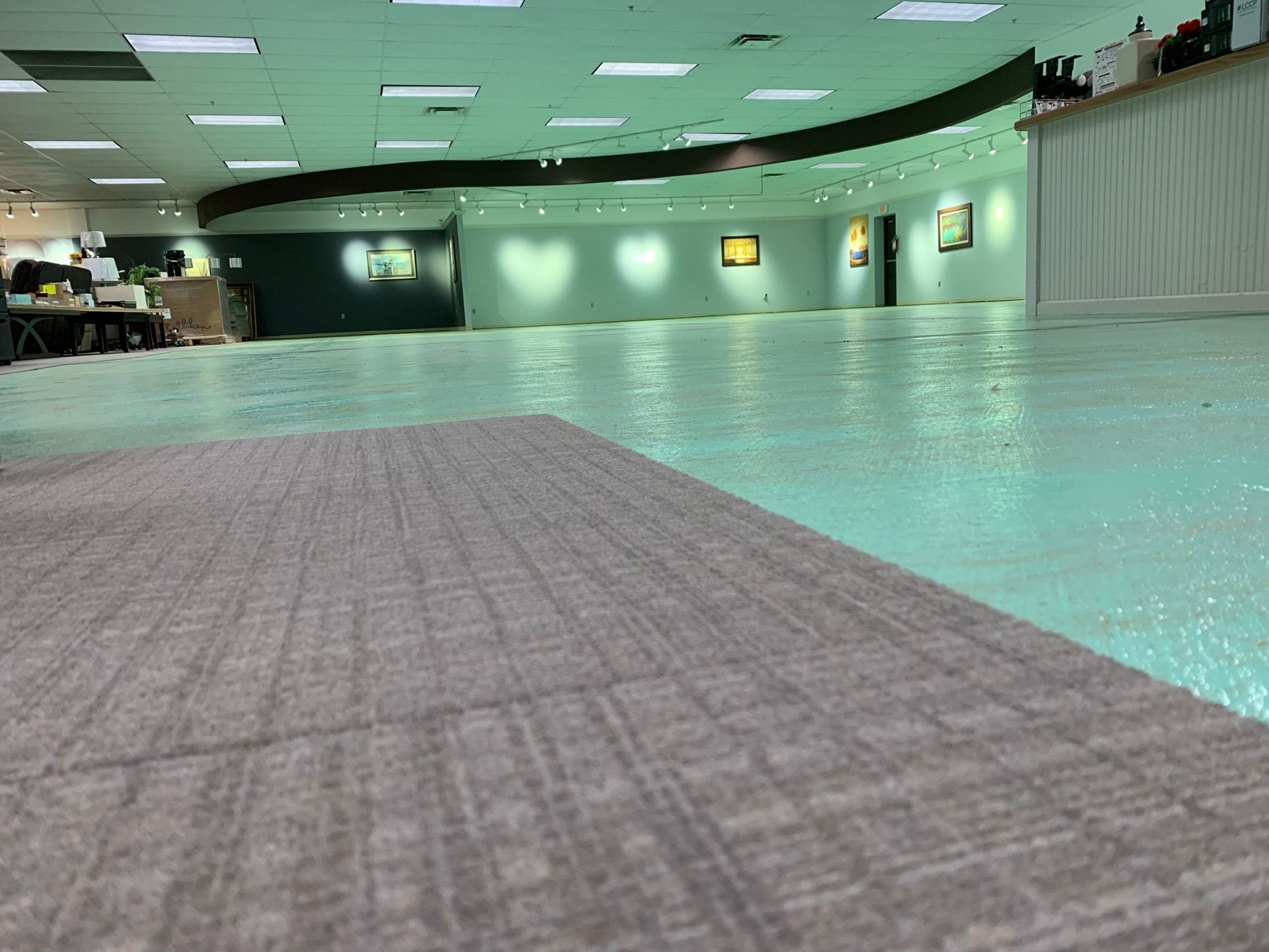 Empty indoor swimming pool with turquoise water and a gray textured deck under green ceiling lights