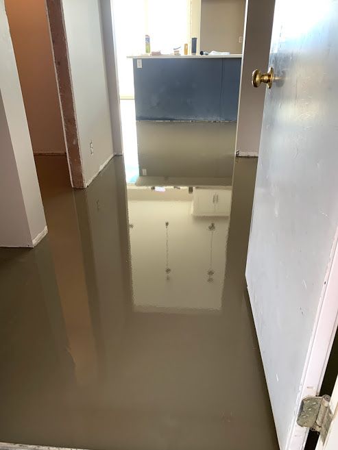 Flooded hallway with standing brown water reflecting a doorway and cabinet area.