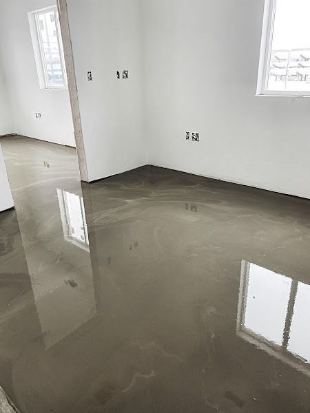 Empty room with glossy gray concrete floor and white walls, reflecting windows and outlets.