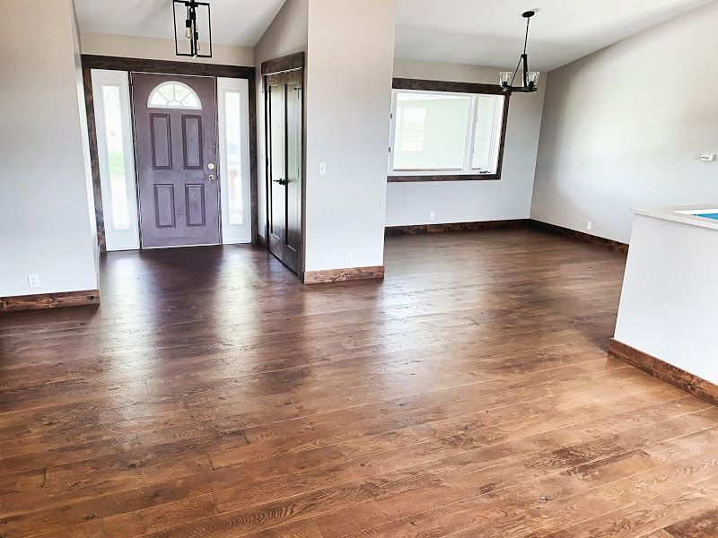 Empty room with wood flooring, front door, and large windows letting in daylight