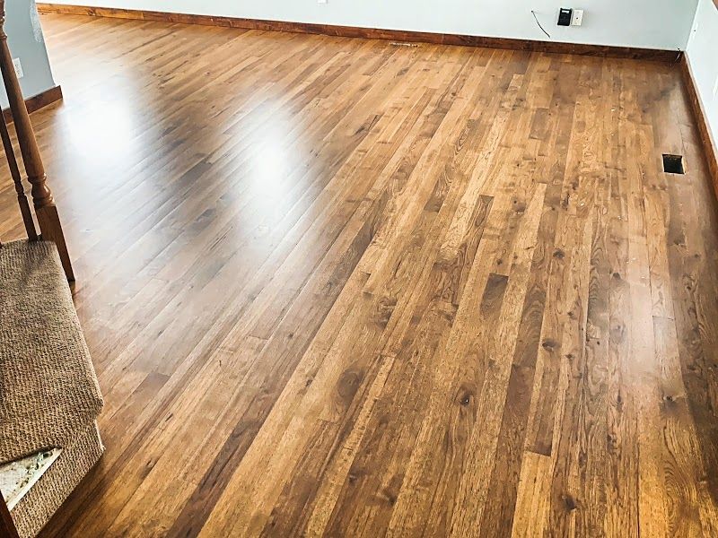 Empty room with glossy wood plank flooring and white walls, reflecting light from a window.