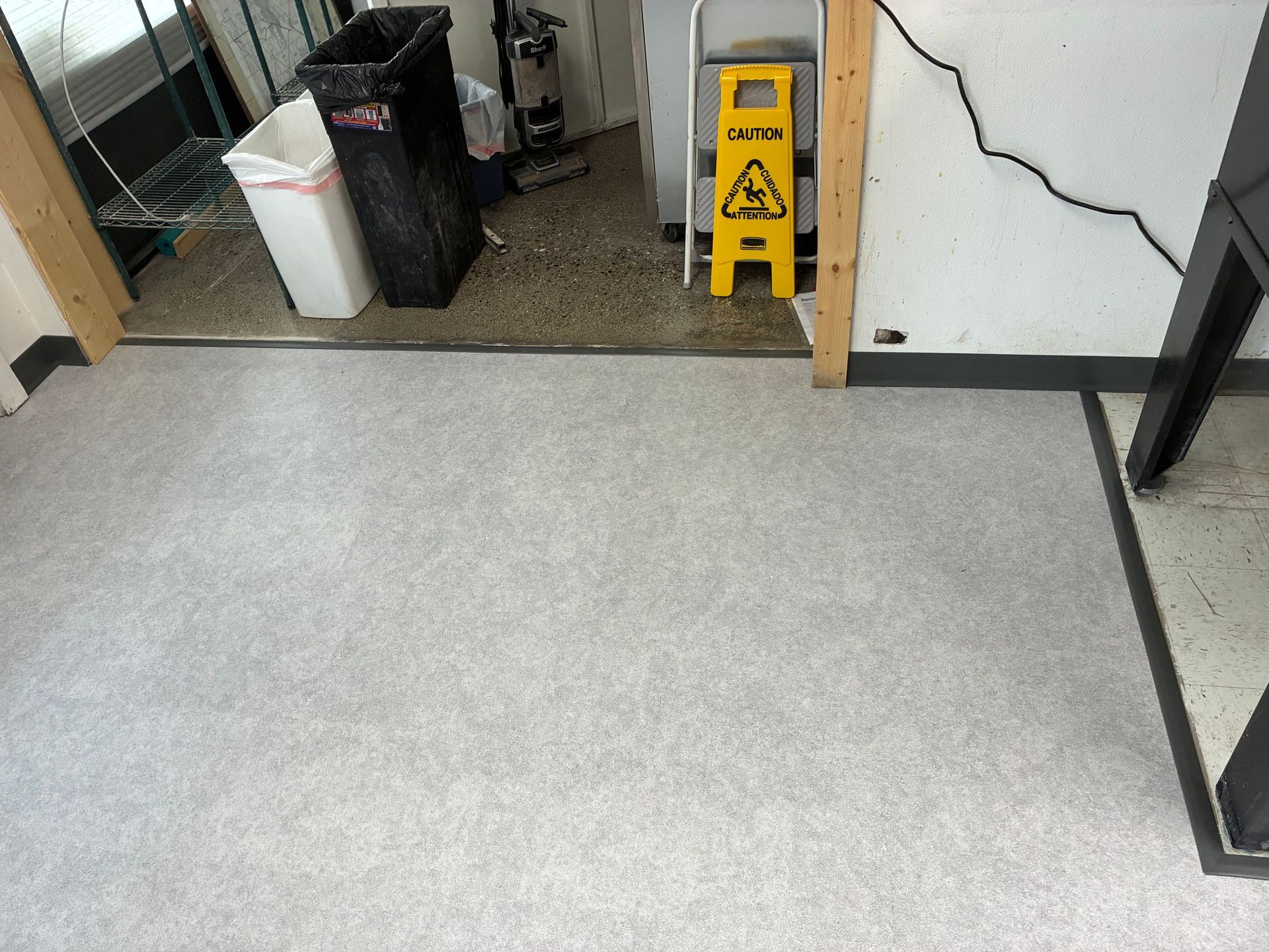 Office entrance with a wet floor sign beside a trash bin and glass door on a carpeted floor.