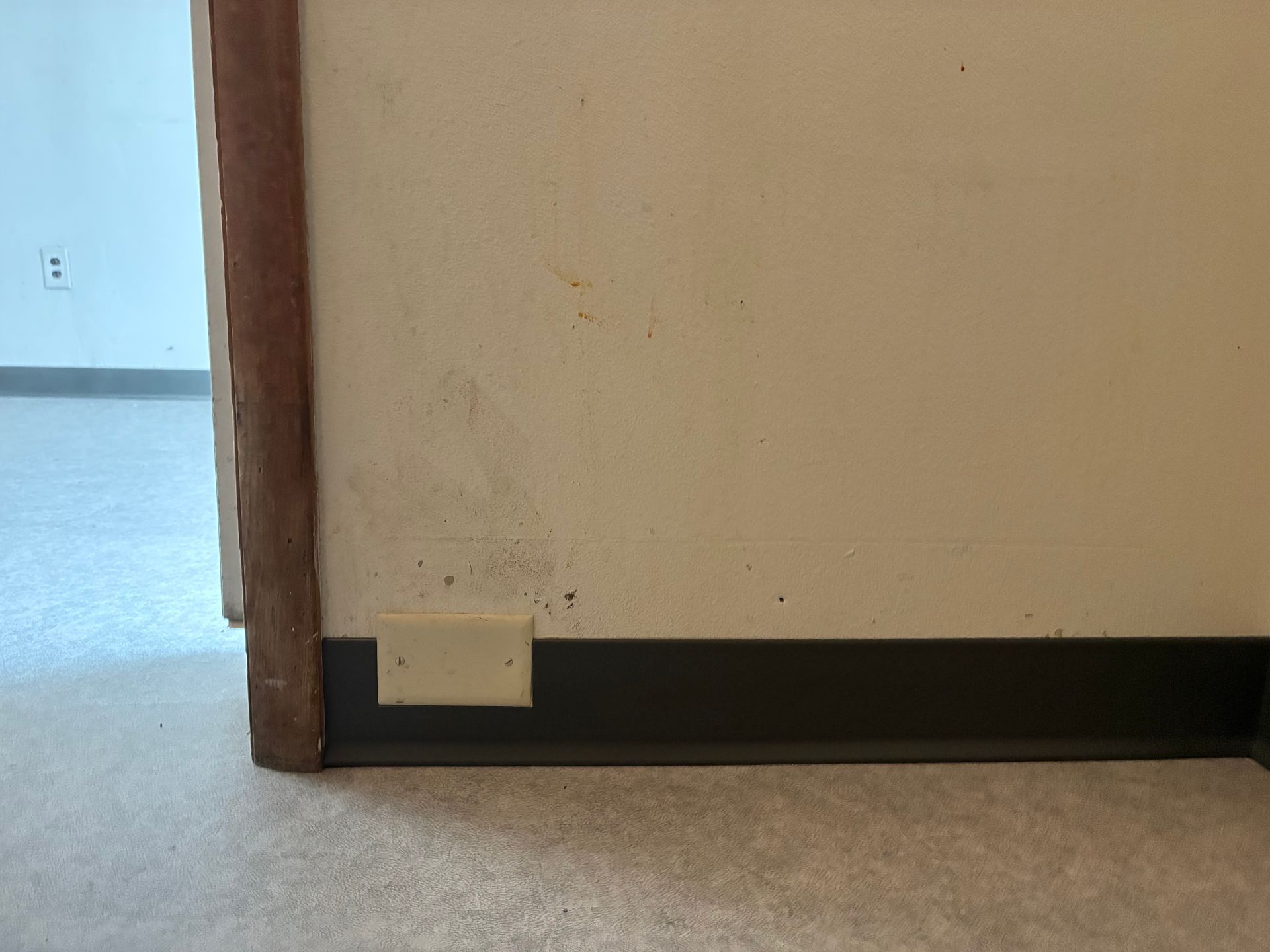 Hallway corner with beige wall, wooden trim, and a small wall-mounted box near the floor