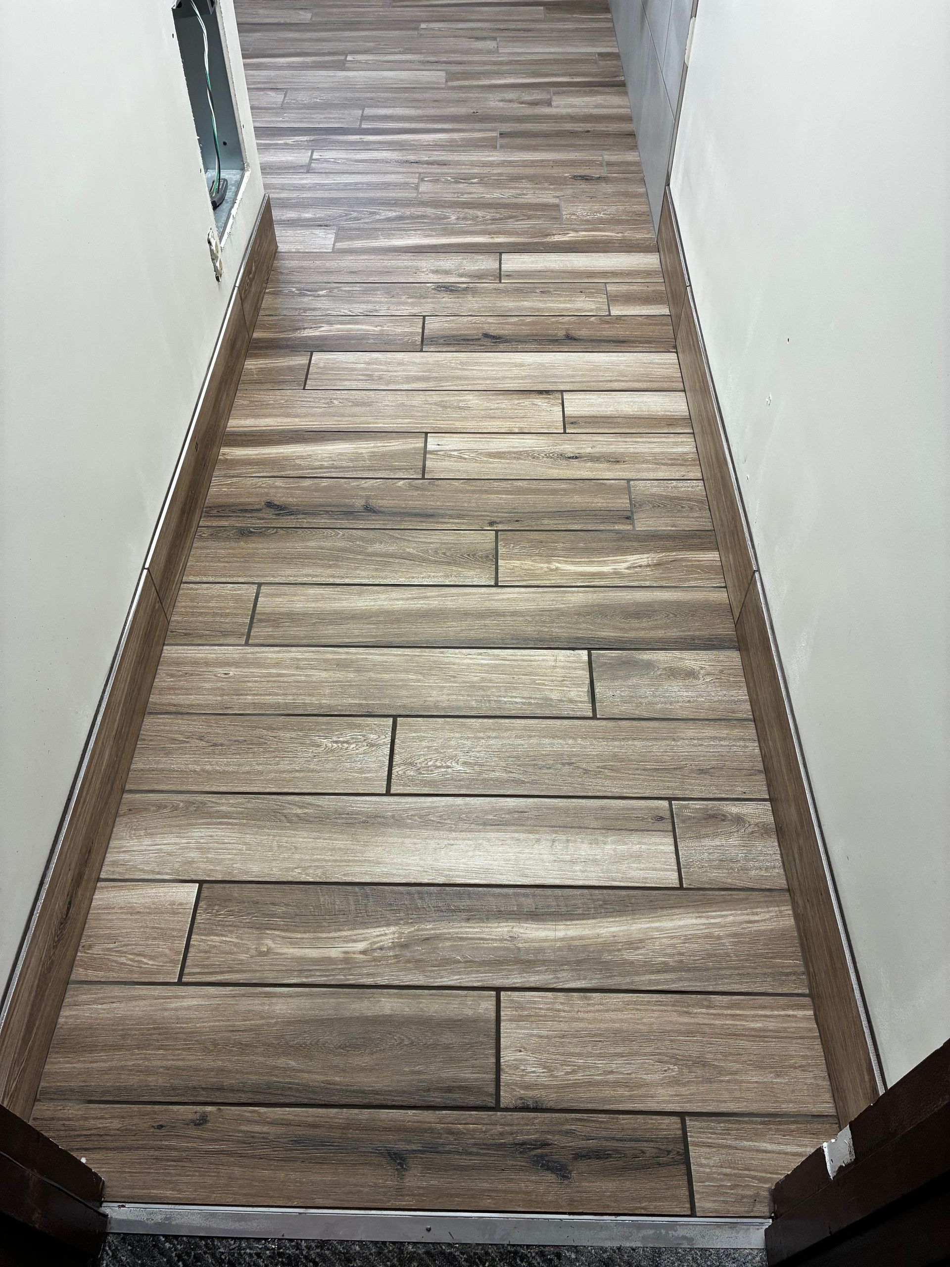 Narrow hallway with wood-look tile flooring and white walls, viewed from above the doorway