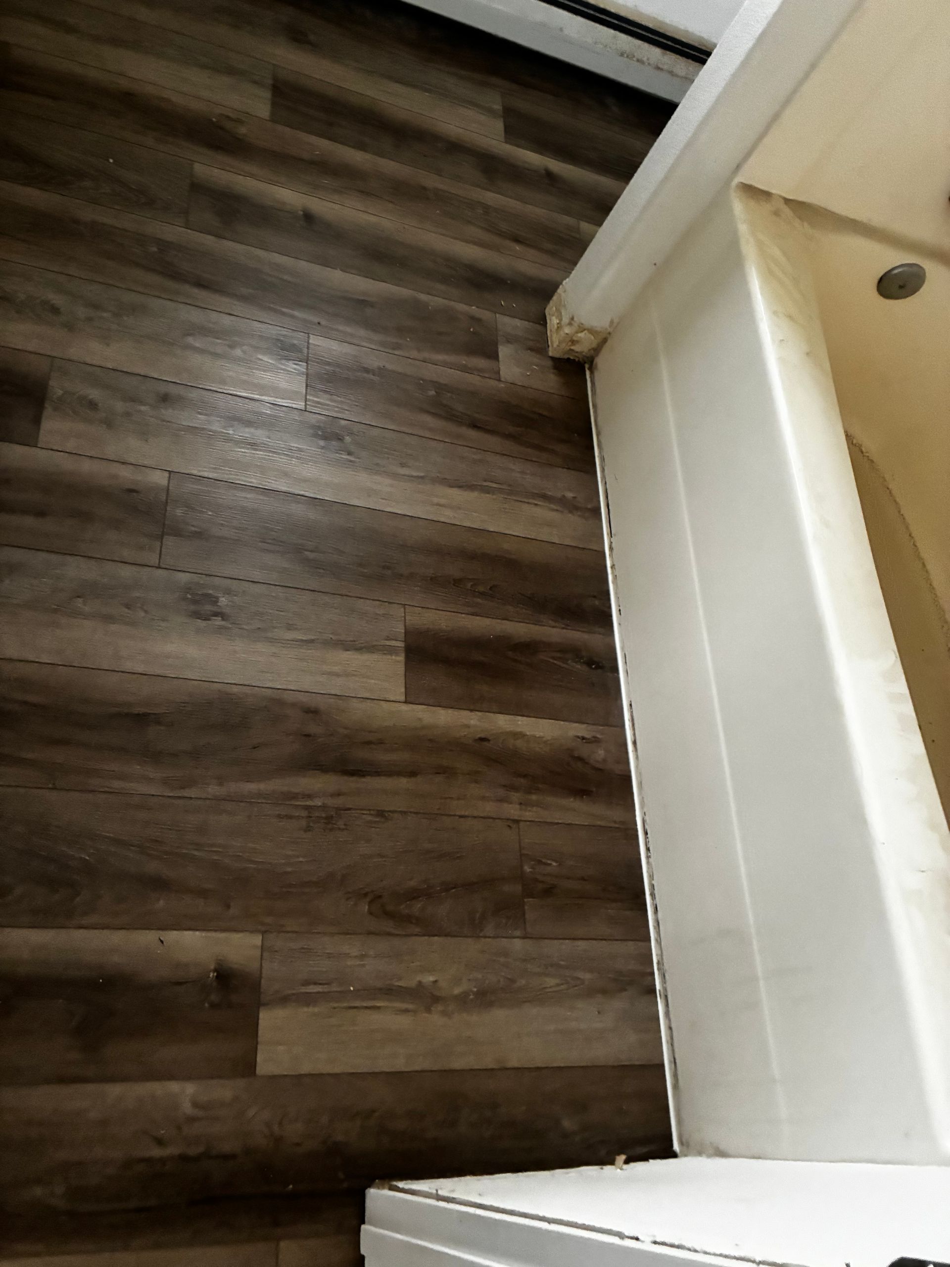 Wood-look vinyl flooring beside a white tiled wall and doorway corner.