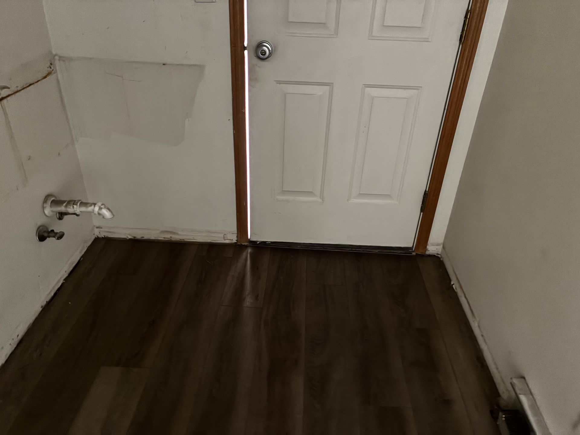 Small room with dark wood floor, white door, and wall fixtures near a sink area
