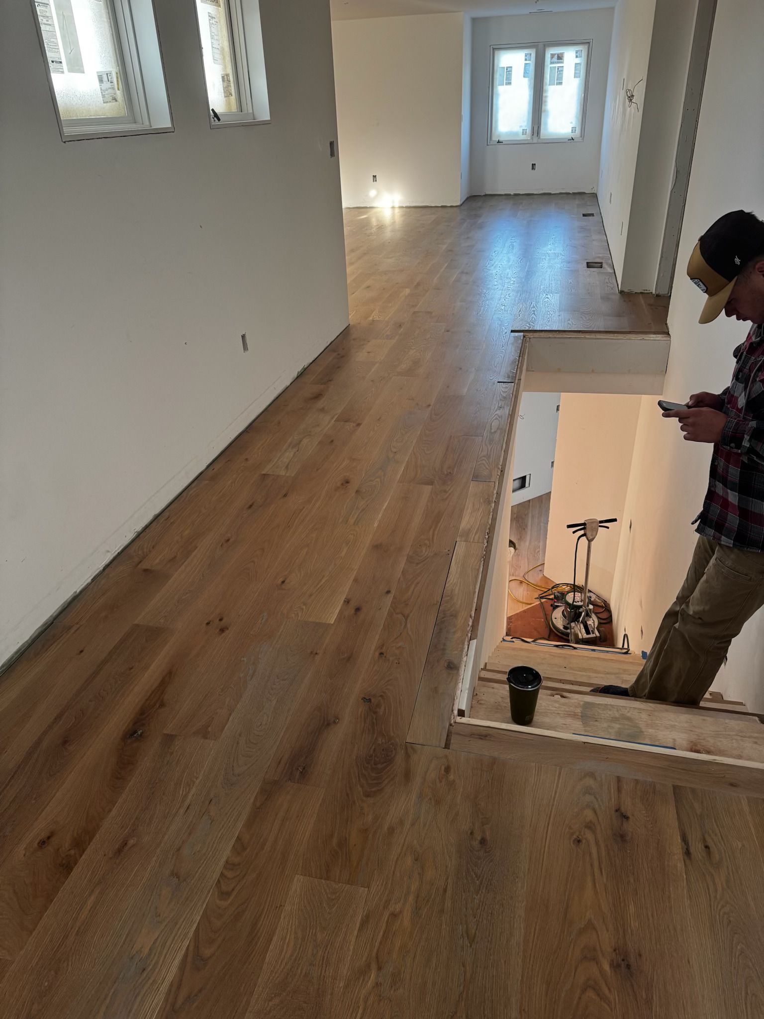 Empty room with wood floors and white walls; a person stands by the staircase opening.