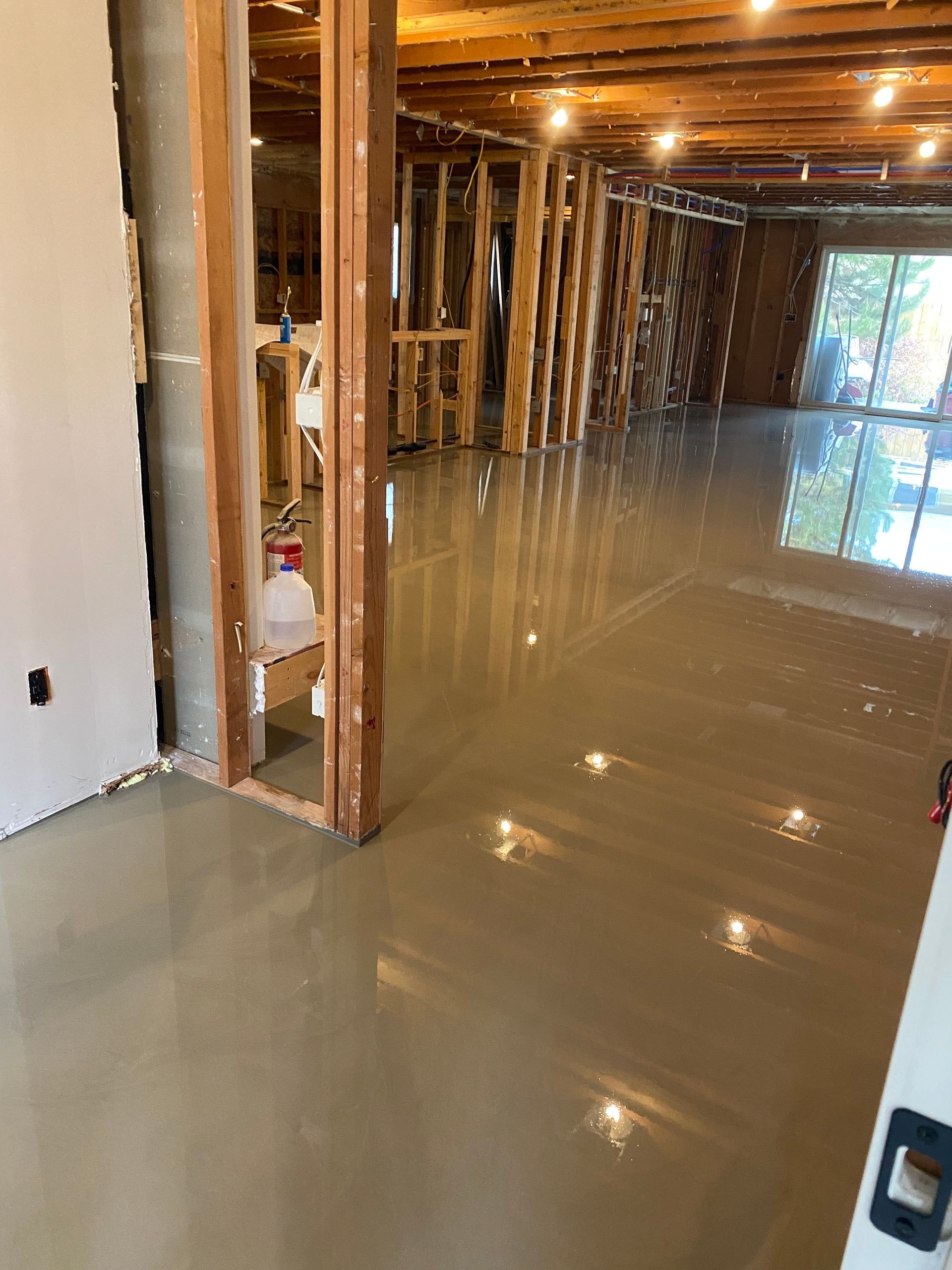 Flooded unfinished basement with standing water reflecting lights and exposed wooden framing.