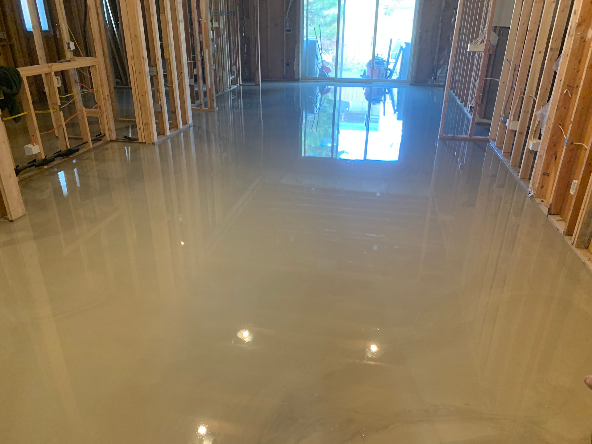 Freshly poured concrete floor in a framed room, reflecting light from an opening at the far end.