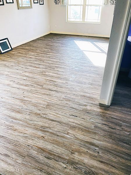 Empty sunlit room with wood-look flooring and white walls, seen from a doorway.