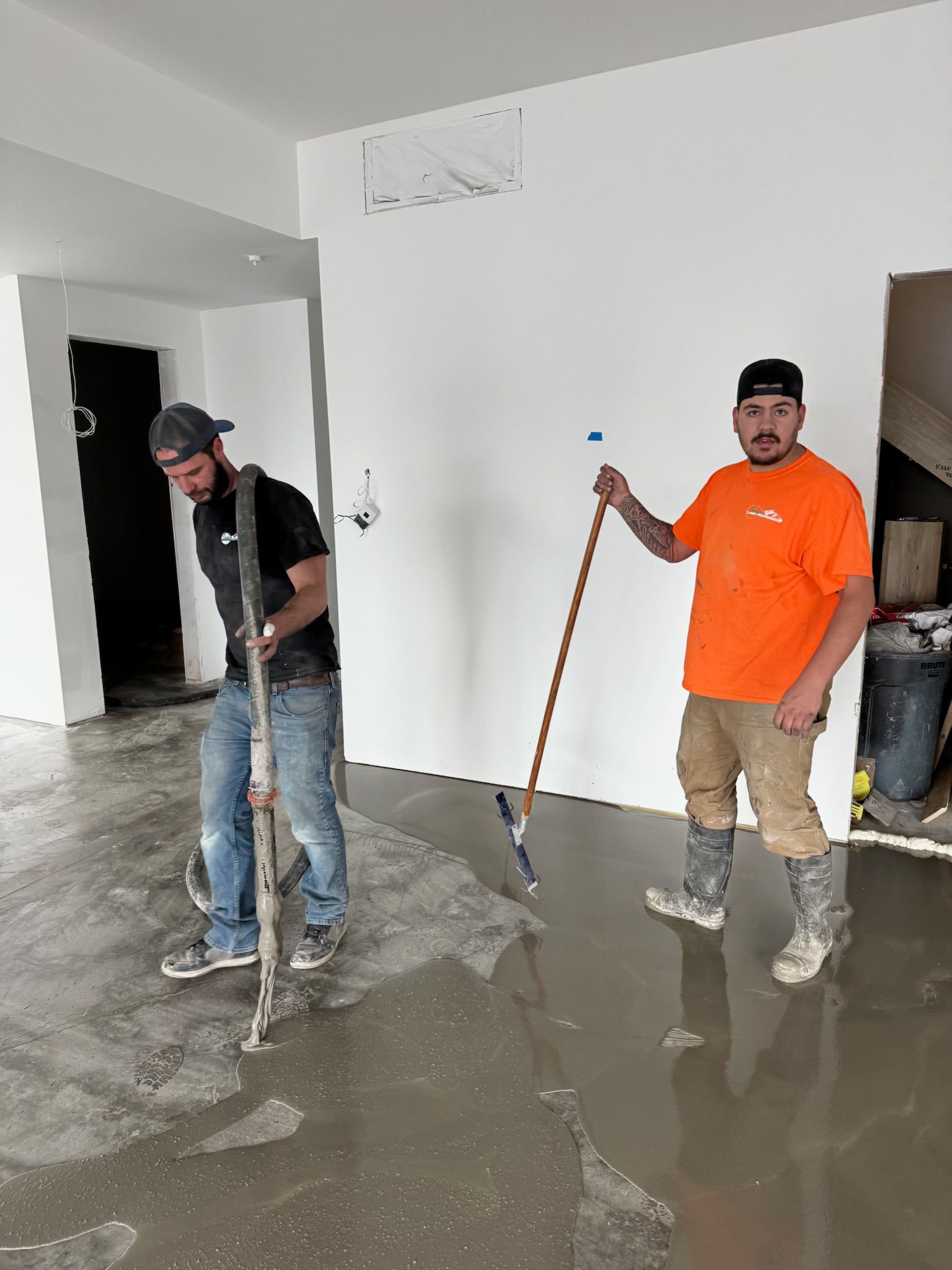 Two workers cleaning muddy floodwater from a room with mops and squeegees