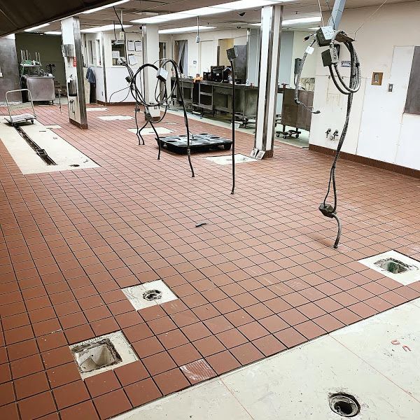 Empty indoor bathroom or locker room under renovation, with exposed pipes and tile flooring.