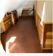 Empty attic hallway with wooden paneling and a tiled floor, lit by sunlight through a small window.