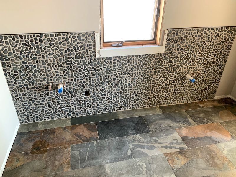 Partially tiled wall in a small room with a window and stone-pattern flooring
