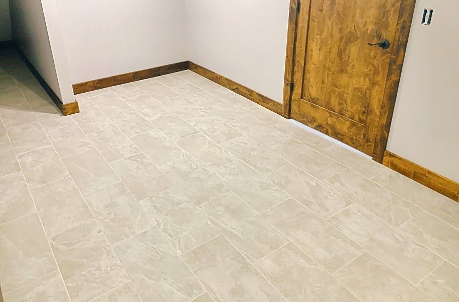 Empty tiled room corner with white walls, wood trim, and a rustic wooden door.